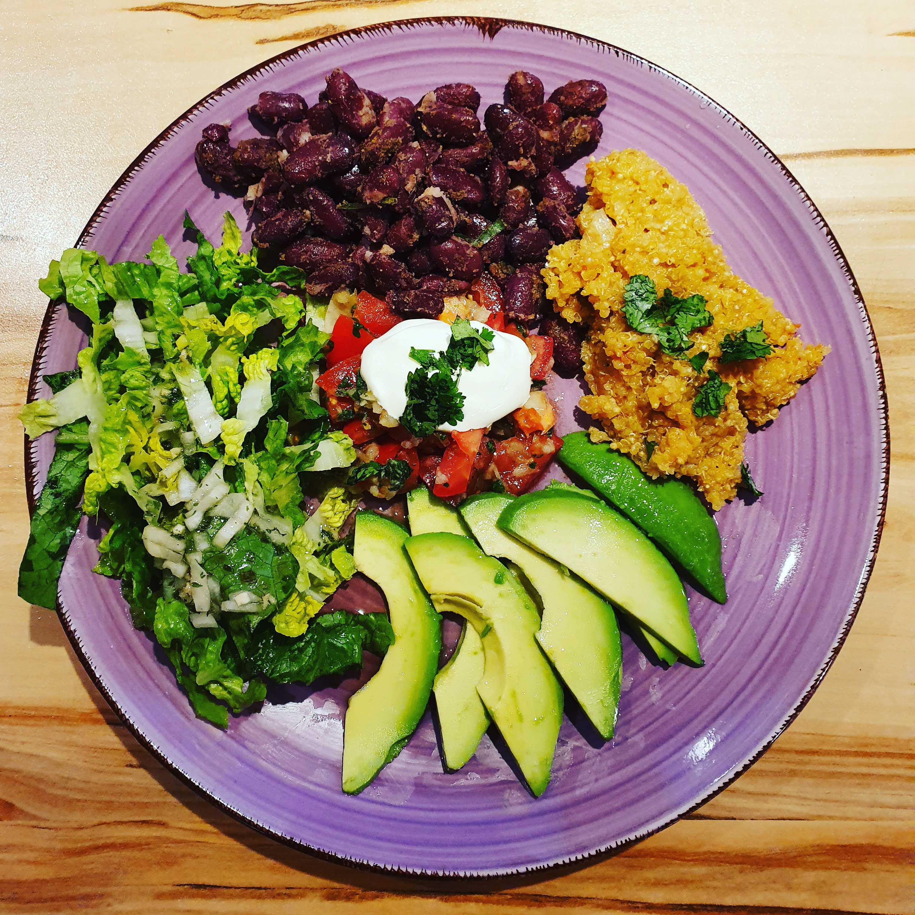 Quinoa-Bowl mit Bohnen, Avocado, Salat und Schmand.