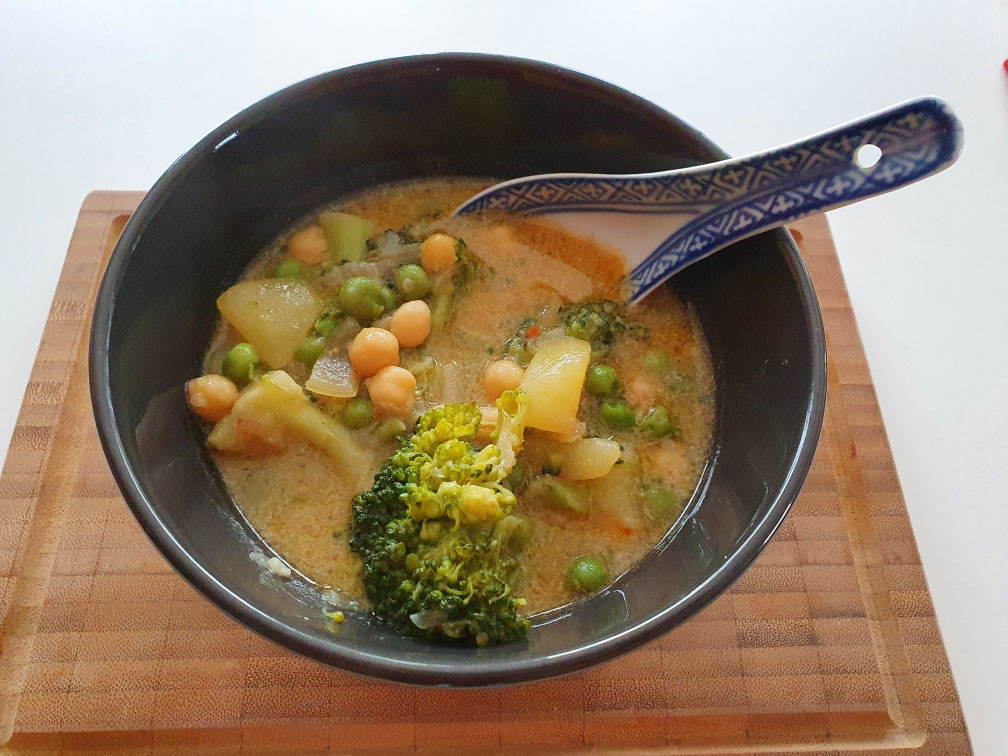 Kokoscurry mit Kichererbsen, Brokkoli und Kartoffeln in schwarzer Schale.