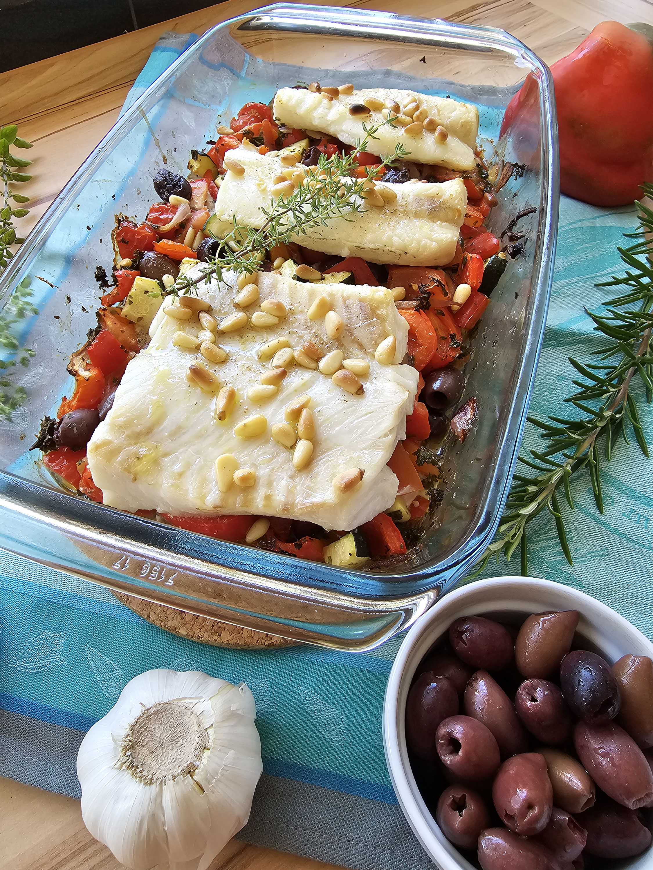 Gebackener Fisch mit Gemüse, Oliven und Pinienkernen.