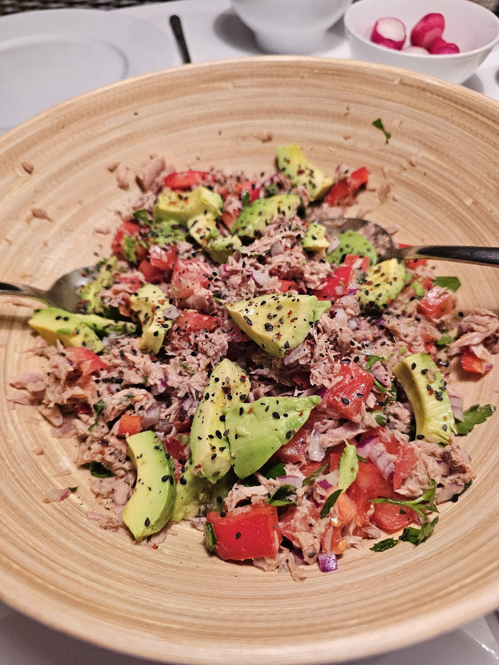 Thunfischsalat mit Avocadoscheiben und Gemüse in einer Holzschüssel.