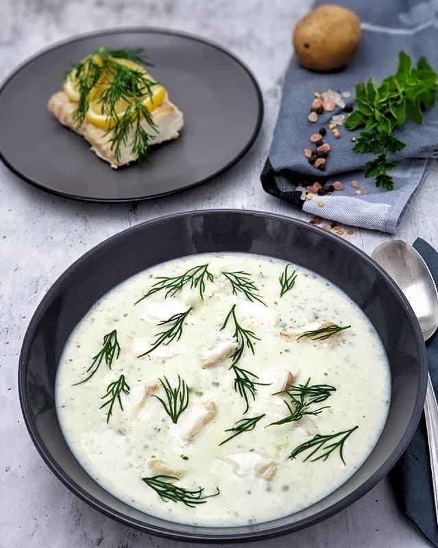 Kartoffelsuppe mit Kräutern und Kabeljau angerichtet in einer dunkelgrauen Schale mit frischem Dill garnieren.