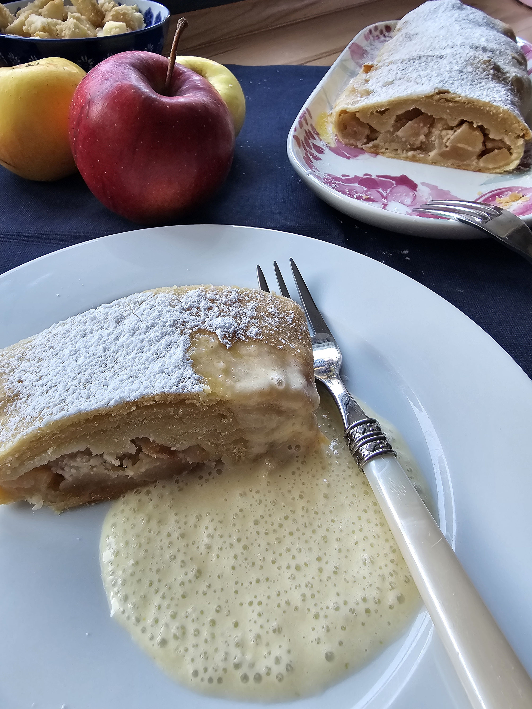 Apfelstrudel mit Puderzucker und Vanillesauce auf einem Teller.