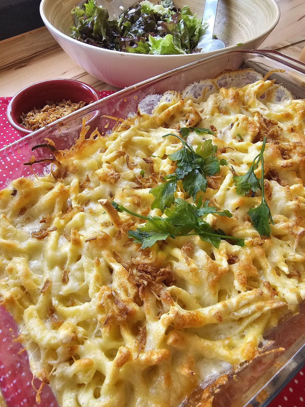 Nahaufnahme von goldbraun überbackenen Käsespätzle in einer Auflaufform mit geschmolzenem Käse und frischer Petersilie.