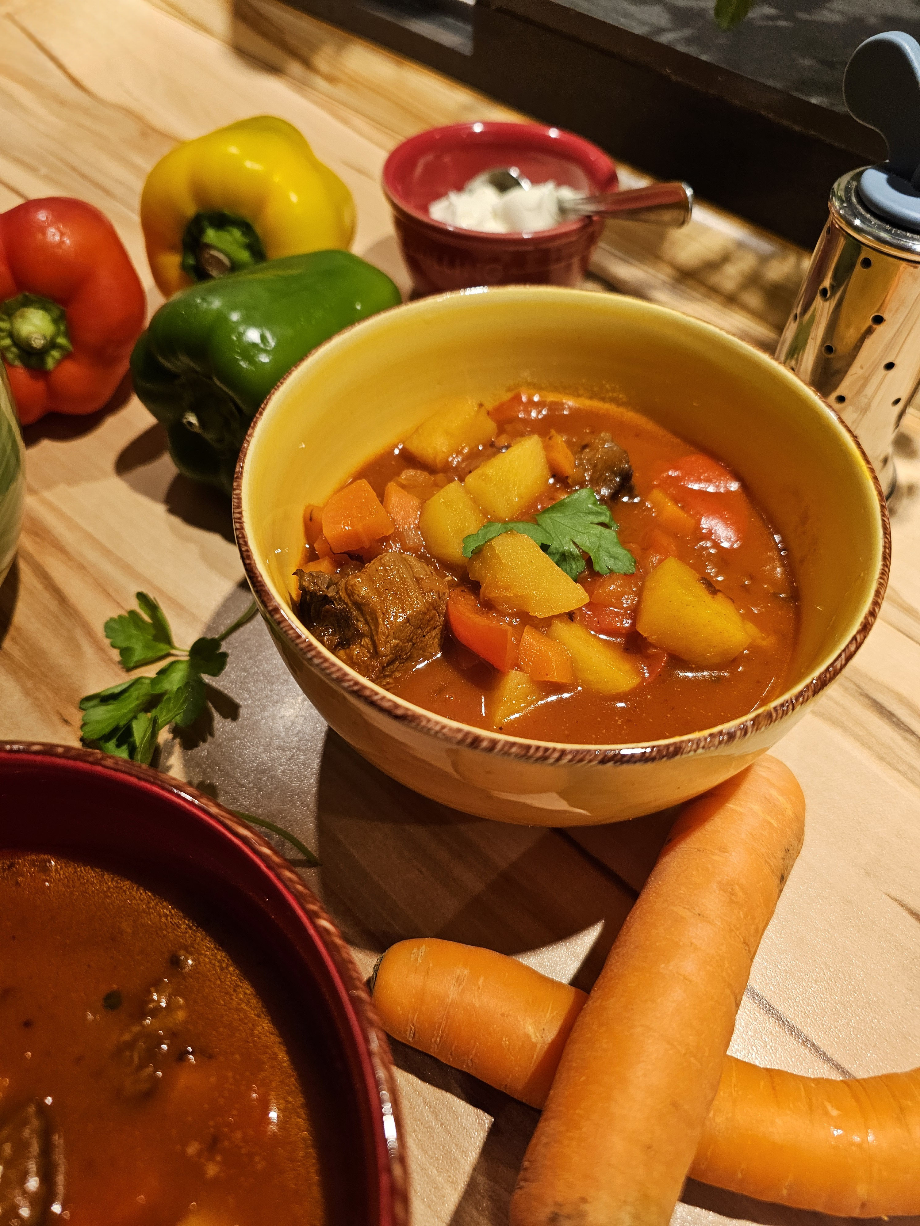 Gulaschsuppe mit Rindfleisch, Gemüse und Petersilie im gelben Suppenteller.