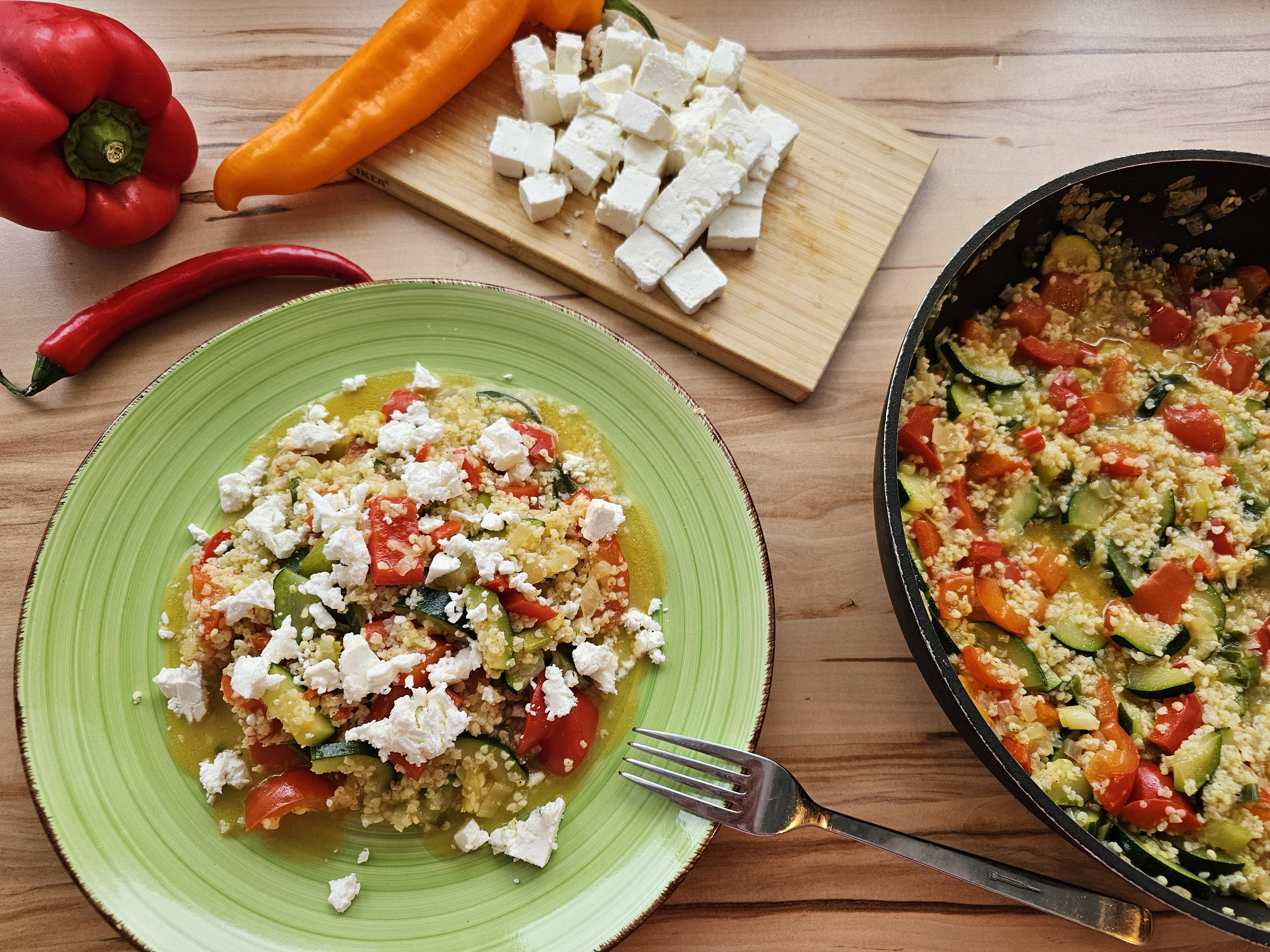 Bunte Hirse-Gemüse-Pfanne mit zerbröseltem Feta auf grünem Teller.