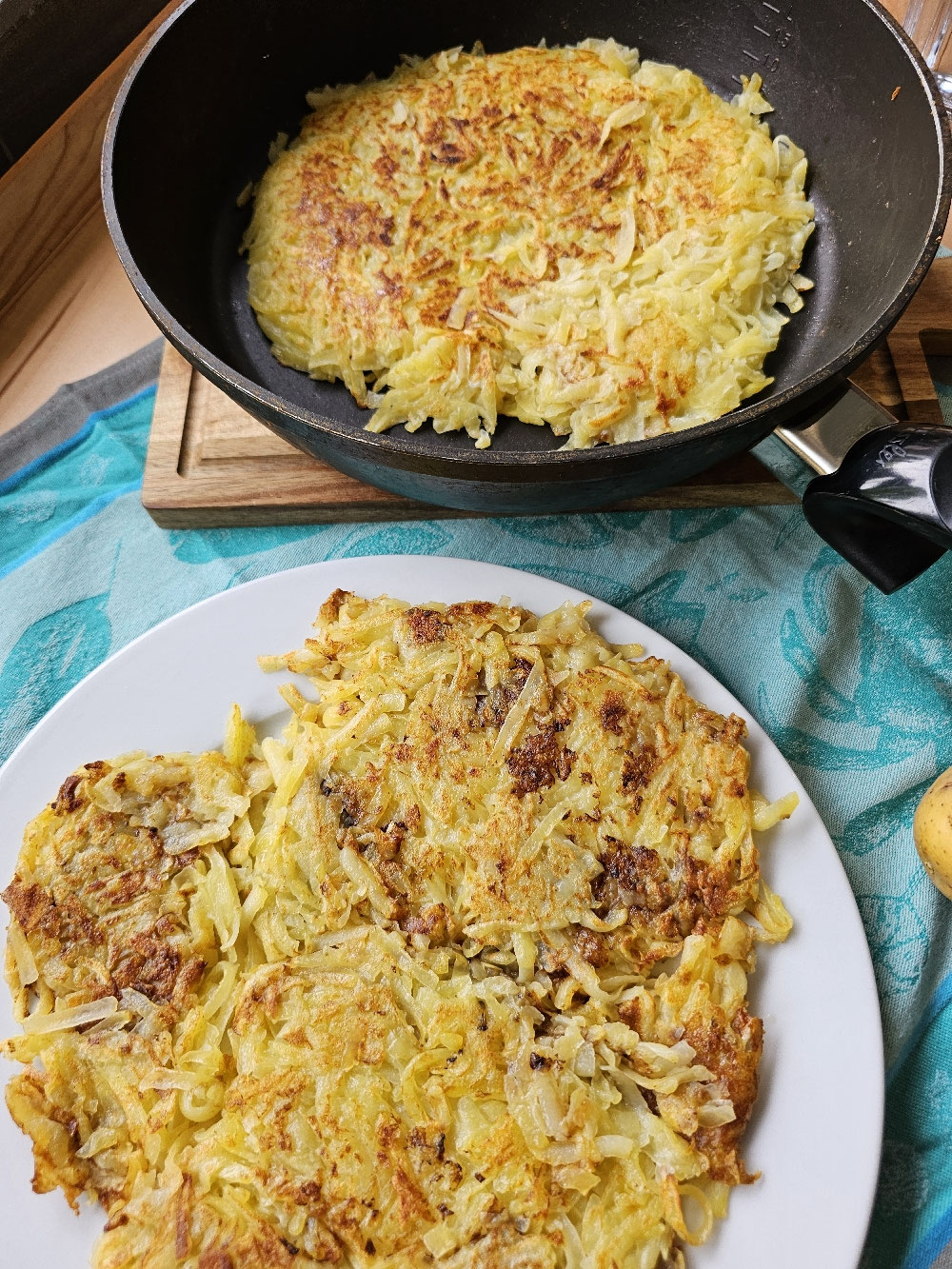 Goldbraune Schweizer Rösti in Pfanne und auf Teller.