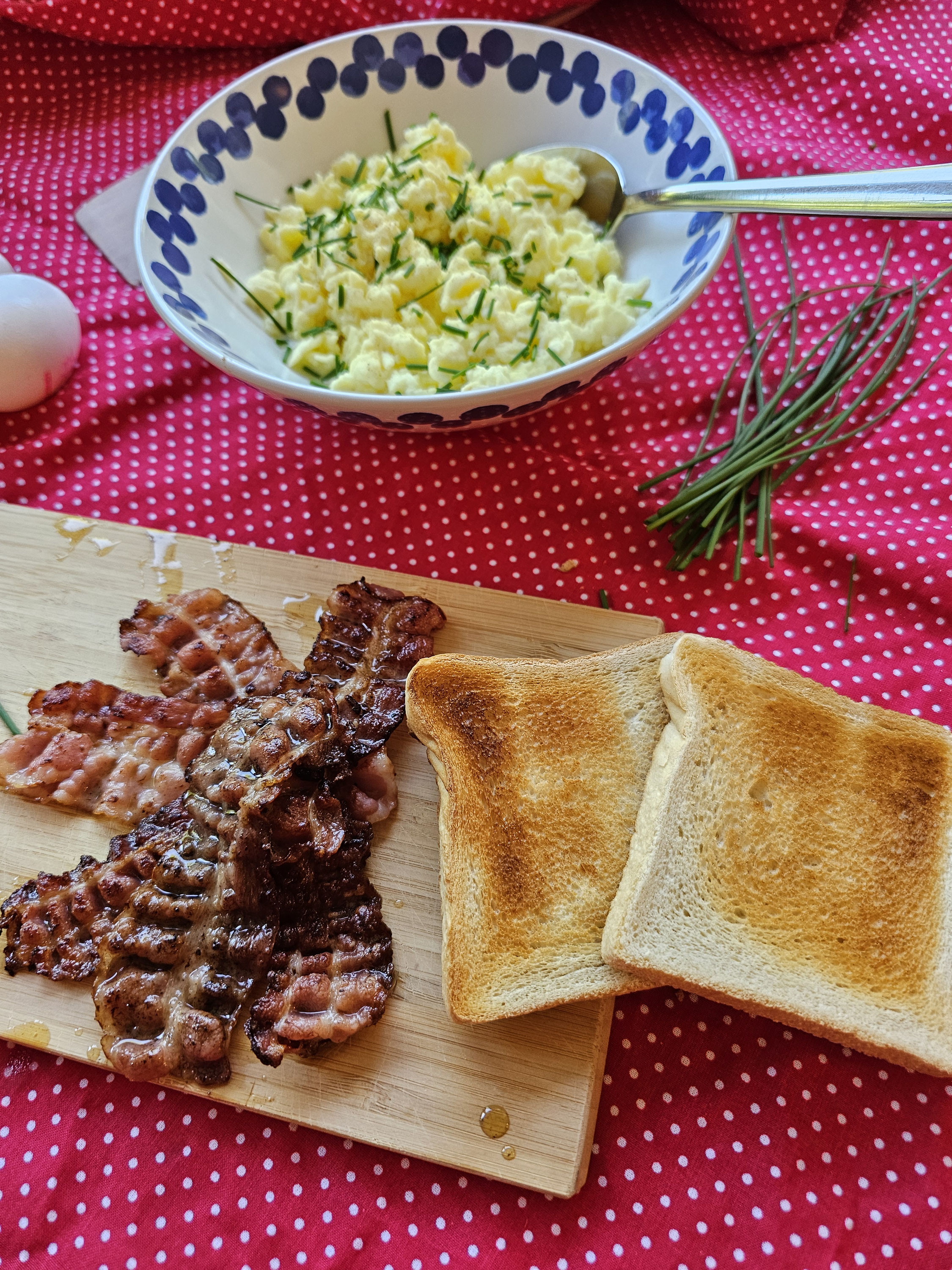 Rührei mit Schnittlauch, knusprigem Speck und Toast als Serviervorschlag.
