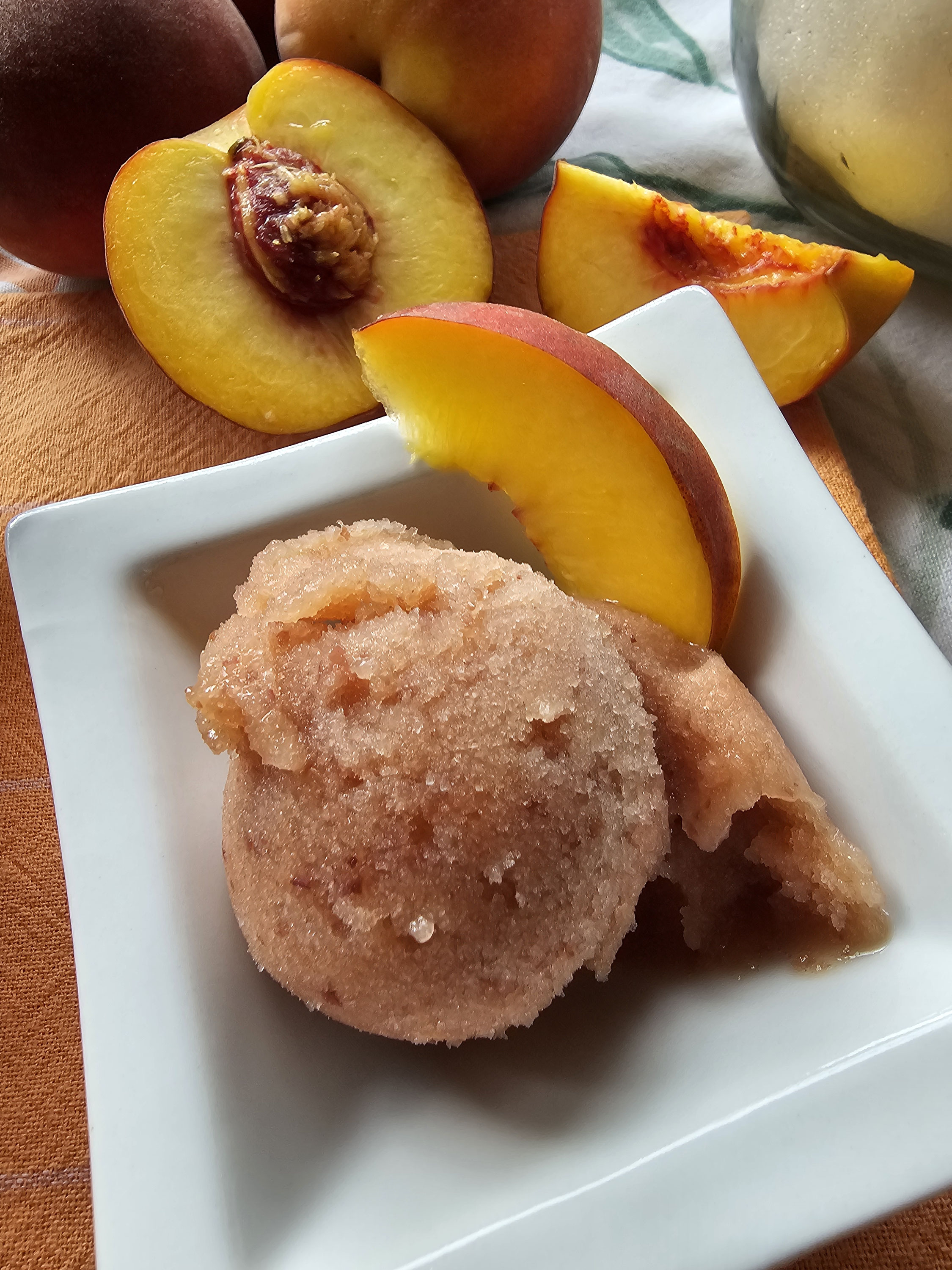Pfirsich-Passionsfrucht-Sorbet auf einem weißen Teller mit Pfirsichspalte.