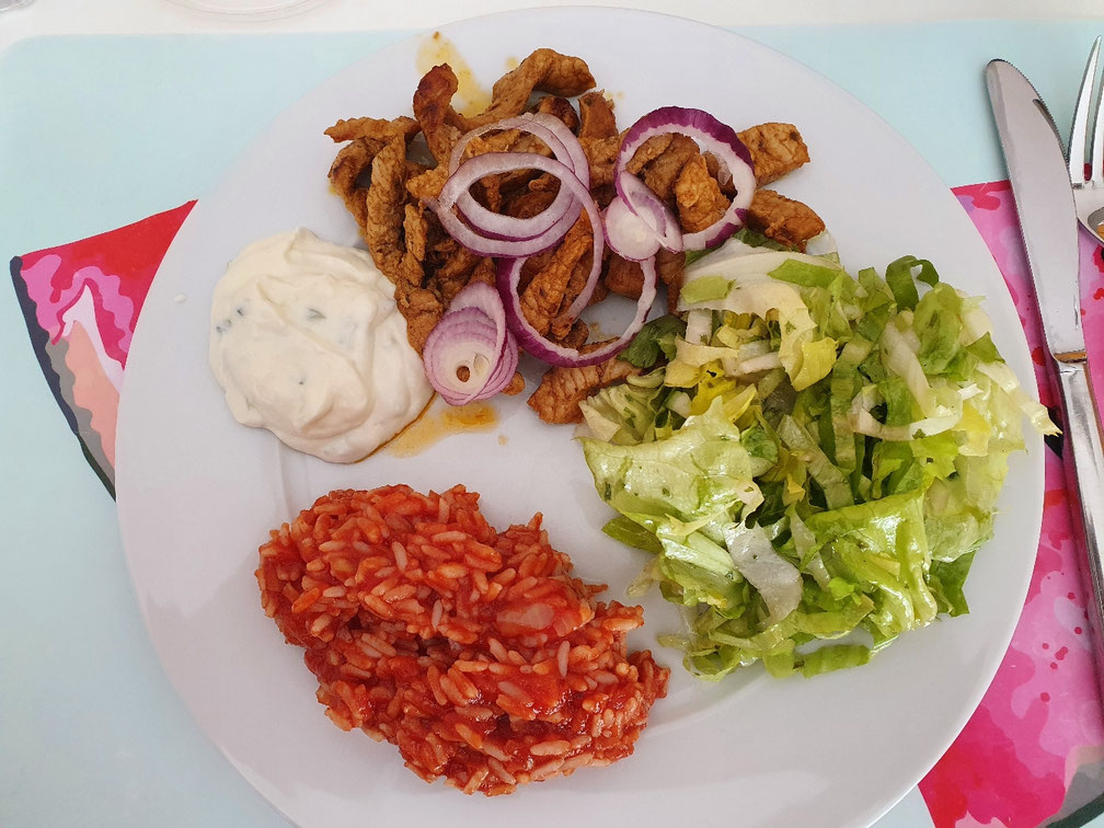 Gyros mit roten Zwiebelringen, Tomatenreis, Tsatsiki und grünem Salat.