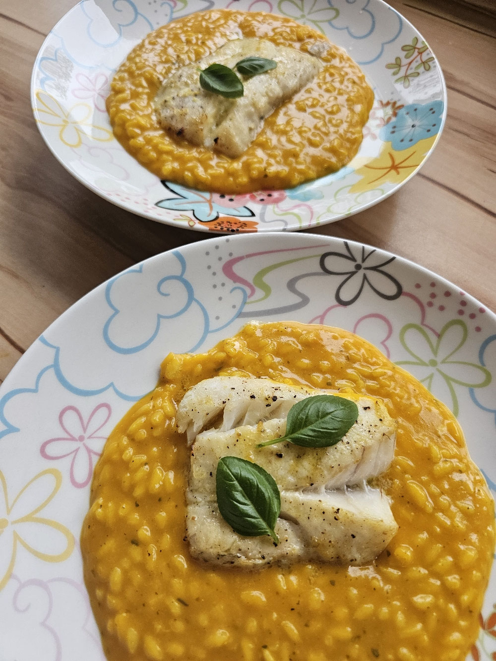 Kürbisrisotto mit Kabeljau auf zwei Tellern.